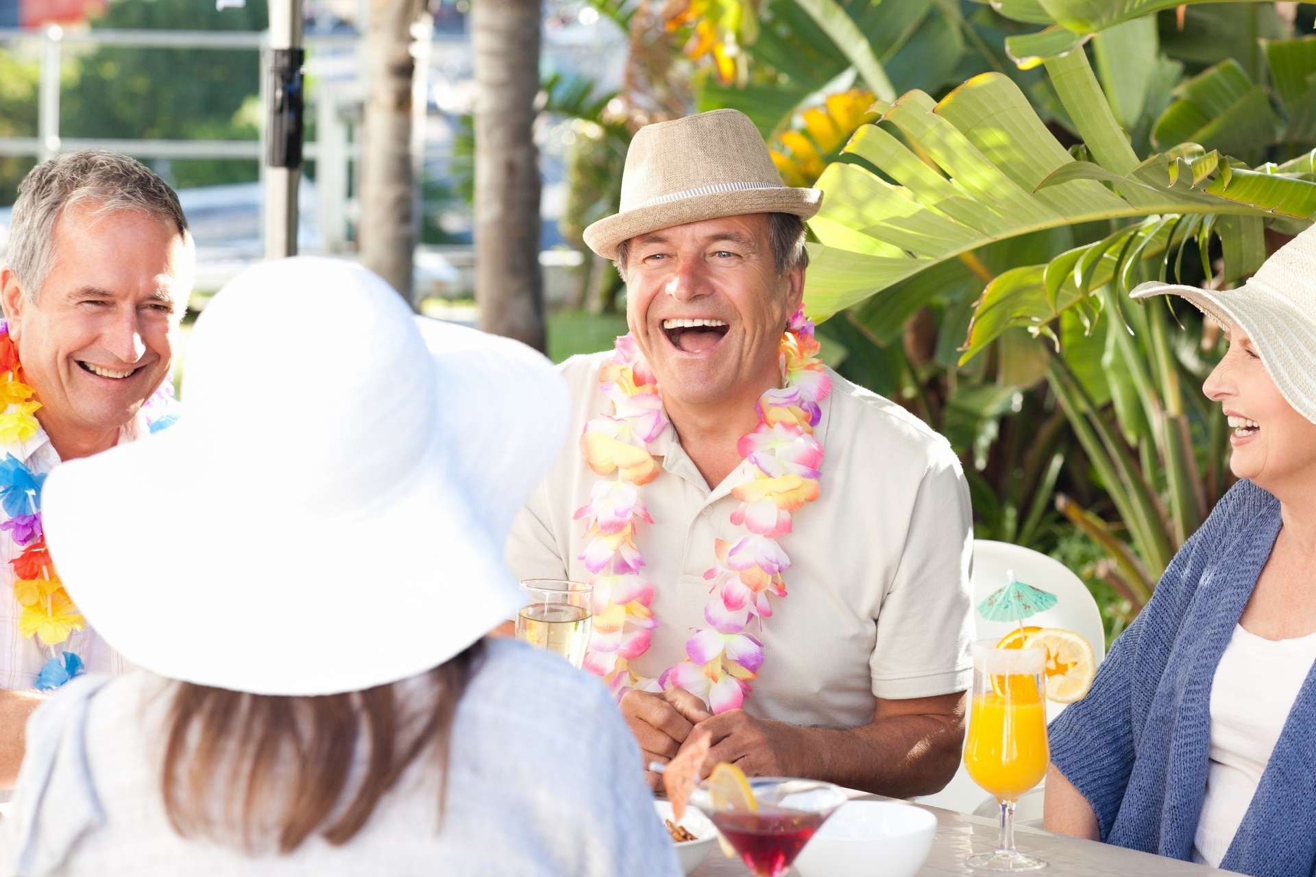 A group of seniors enjoying tropical drinks and wearing leis, laughing together.